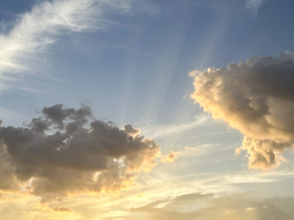 A vibrant sunset casts a warm orange glow on unique cloud formations, creating a striking contrast with the remaining patches of blue sky.
