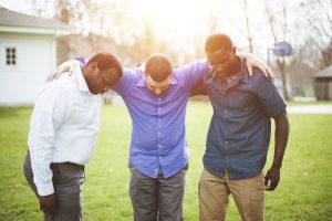 A group of diverse friends with hands on the shoulders looking down and praying together